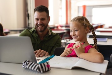 Young school teacher helping girl with study on laptop in