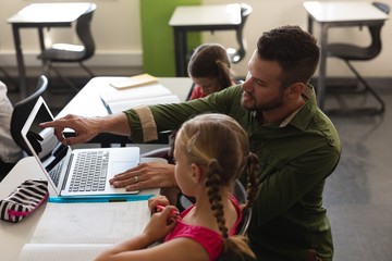 Young school teacher helping girl with study on laptop in