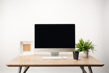 workplace with coffee to go, photo frame, green plant and desktop computer with copy space isolated on white