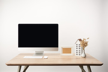 workplace with house model, dry flowers, photo frame and desktop computer with copy space isolated on white