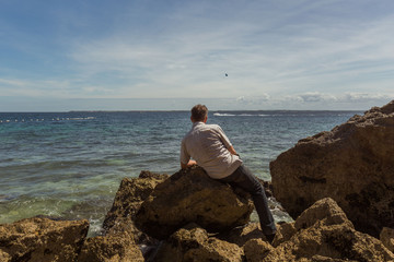 one man alone sitting on a  rock enjoy the view to the sea and islands with boats and recreation activities parasailing 