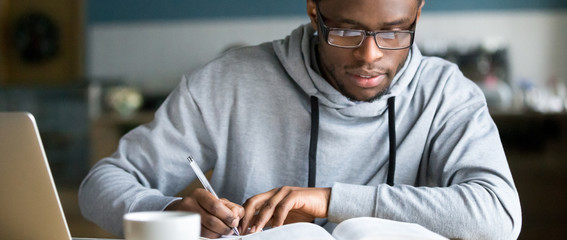Closeup smart millennial african student wear glasses hold pen noting writing down information...