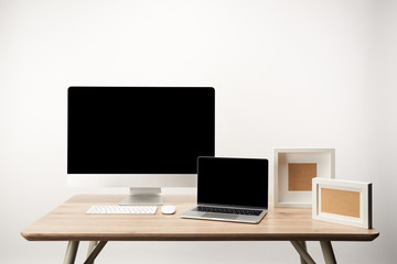 workplace with photo frames, desktop computer and laptop with copy space on wooden table isolated on white