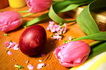 Obraz na płótnie Canvas Close up beautiful naturally colored Easter egg on wooden table with pink flowers. Eggs painted with onion skins. Easter holiday concept. 