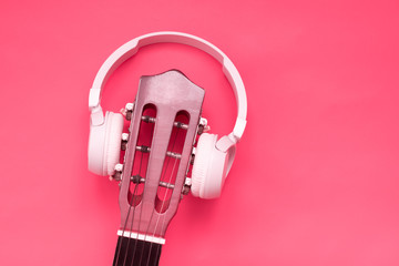 Classic guitar and modern headphones on pink background. music listening concept