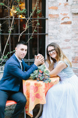 Elegant young couple in blue clothes celebrating wedding and walking streets in Sirmione. Young couple sitting at the table of street cafe in Sirmione, Italy