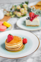 pancakes with tea, cheesecake and biscuits on a marble table with flowers
