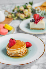 pancakes with tea, cheesecake and biscuits on a marble table with flowers