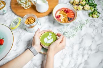 green tea latte in the hands of a girl on the table with oatmeal and flowers