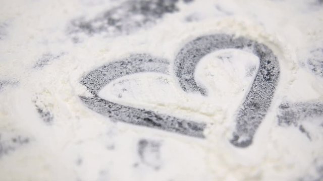 close up drawing heart on sprinkled flour black table top/ preparing for cooking 