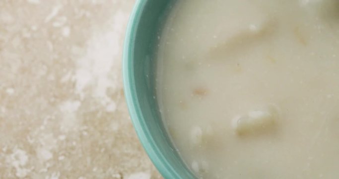 Close video of slowly stirring canned clam chowder with a spoon in a green bowl then taking a spoonful at the end.