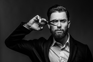 Barbershop advertising concept. Businessman with serious face isolated on black background. Man with long beard holds steel scissors. Man formal suit cuts beard and moustache.