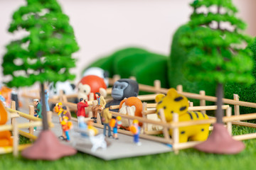 A self constructed miniature toys concept of people at the zoo - school kids, old people sitting on benches and a photographer dangerously takes photos of his friend on a fence.