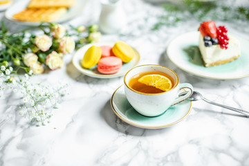 cup of tea with lemon, cheesecake and macaroons on the table