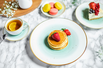 pancakes with tea, cheesecake and biscuits on a marble table with flowers