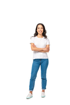 Smiling asian young woman in white t-shirt and blue jeans standing with crossed arms isolated on white