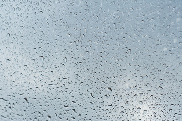 closeup of rain drops on window on cloudy sky background