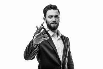 Young handsome bearded man with long beard moustache and brunette hair holding pointed hairdresser or barber scissors in studio on grey background