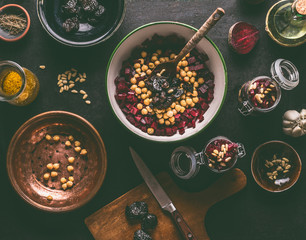 Healthy vegan beetroot salad preparation with chickpeas and pine nuts on dark kitchen table...