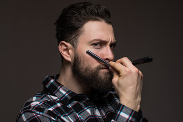 Handsome hipster man with long beard hold a razor vear the face wear in plaid shirt isolated on gray background