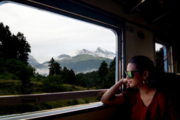 Young beautiful Asian woman wearing sunglasses traveling by train sitting near the window and looking through the train window.