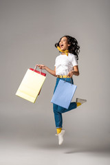 Beautiful young asian woman jumping up with happy smile while holding colorful shopping bags on grey
