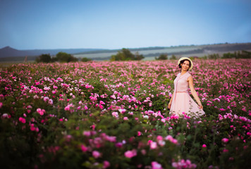 Fototapeta na wymiar Beautiful young woman walking near roses in a garden. The concept of perfume.