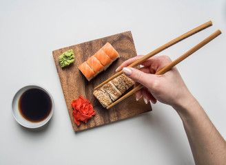 girl eating an appetizing sushi set with ginger, soy sauce and wasabi on a white background