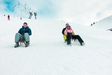 Fototapeta na wymiar Happy friends having fun with sledding on snow high mountains