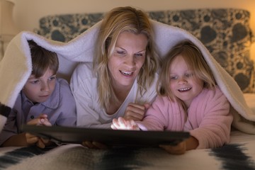 Mother with her children using digital tablet under blanket in