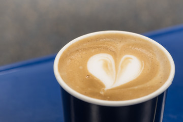 Food and Drink concept. Close up of paper cup of hot coffee with milk foam with latte art heart shape.