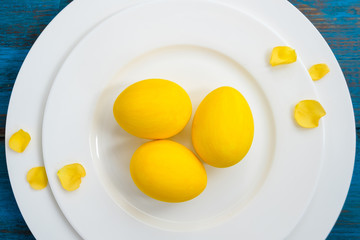 Easter table setting on blue wooden background with yellow spring flowers and eggs.