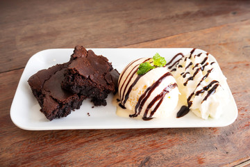 Homemade brownie served with vanilla ice cream and whipped cream on white plate. Sweet dessert with cocoa and coffee.