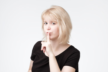 ovely blonde female asks to keep secret information confidential, dressed in black t-shirt