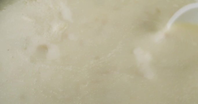 Close video of slowly stirring canned clam chowder with a white spoon then taking a spoonful at the end.
