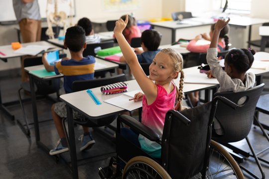 Smiling disable schoolgirl looking at camera and raising hand in