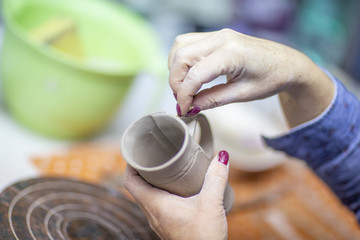 Hands of artist who make a mug from ceramic clay in studio