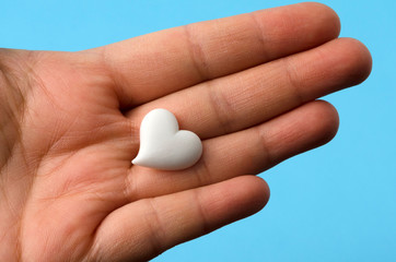 Hand holding a little white heart against blue background