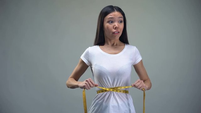 Obsessed woman tightening measuring tape on her waist desire to be slim, bulimia