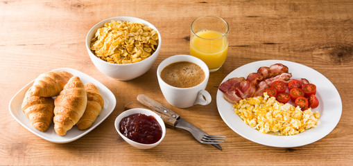 Breakfast with scrambled eggs, bacon, tomatoes,coffee,orange juice ,croissant and corn flakes on wooden table. Panoramic view