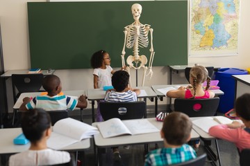 Rear view of little schoolgirl explaining human skeleton model