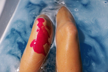 Top view knees in bath with azure water and bath bomb and pink blot