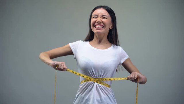 Young woman tightening measuring tape, torturing herself with diet, bulimia