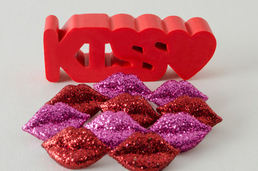 Kiss word in red with a little heart and little shinny red and purple lips against white background
