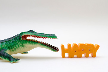 Rubber toy crocodile next to the word happy against white background