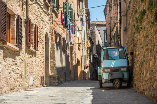 A picture from the old Italian Tuscan town Volterra. The traditional old scooter is standing in the lonely street with stone houses.
