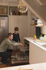 Father and son putting utensils in dishwasher