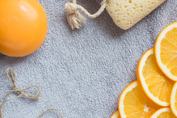 Fresh orange scented background for bathing theme: the big orange soap, the slices of orange and the bath sponge on the gray bath towel