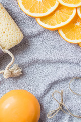 Fresh orange scented background for bathing theme: the big orange soap, the slices of orange and the bath sponge on the gray bath towel