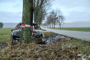 Car destroyed during the traffic accident. It was caused by the bad weather conditions in winter, because of the black ice or snow. The car is burnt, abandoned and stands by the road in the snowfall.